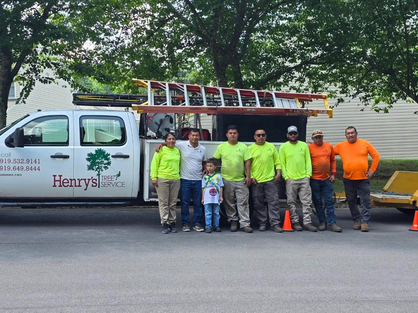 Team of Henry's Tree Service standing in front of their truck, showcasing their commitment to tree care and professionalism, wearing bright safety gear.