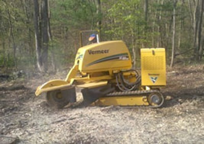 Stump grinding machine by Vermeer in a wooded area, demonstrating stump removal process for landscape improvement after tree removal.